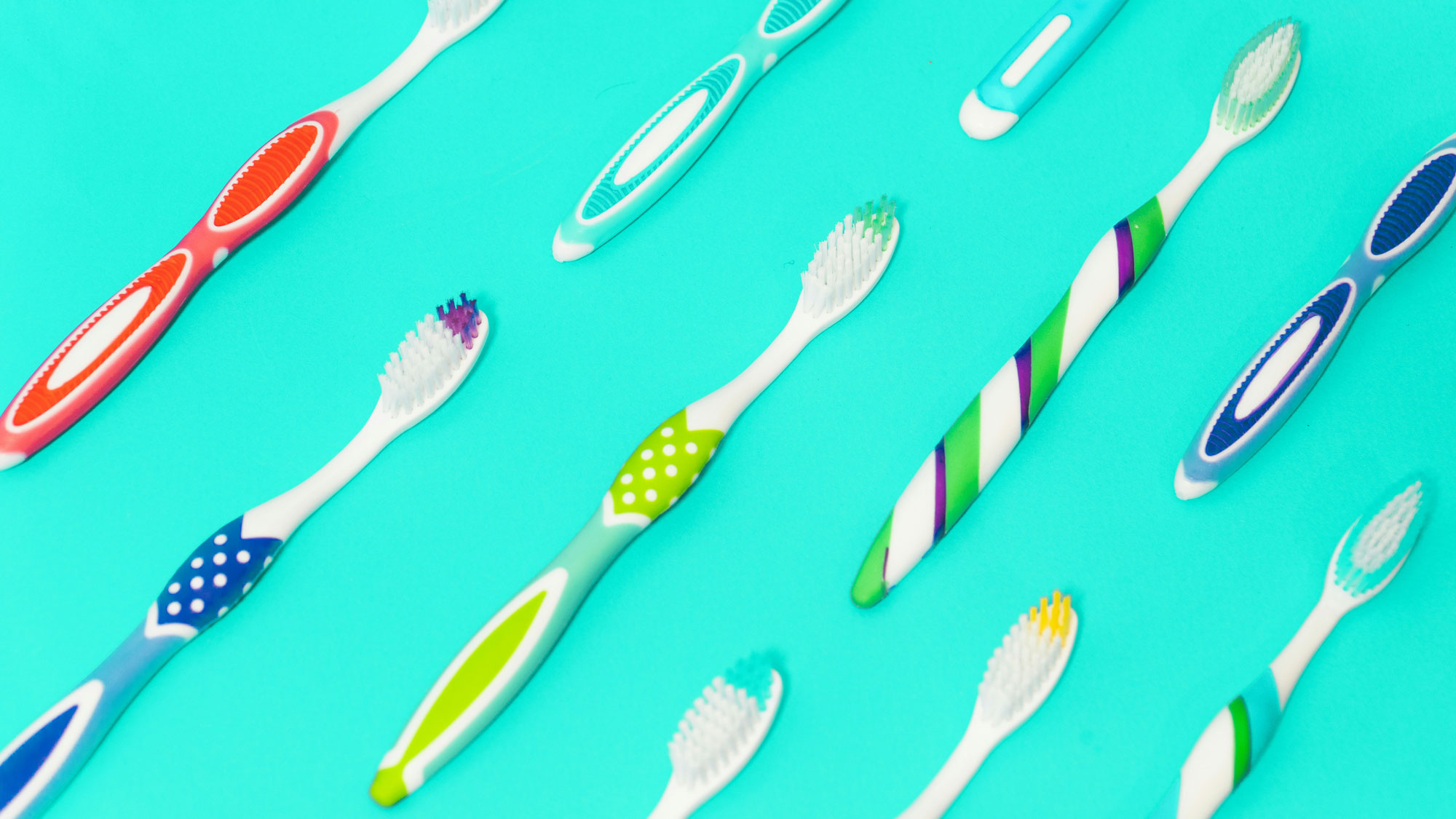 colorful toothbrushes lined up diagonally on a cyan background