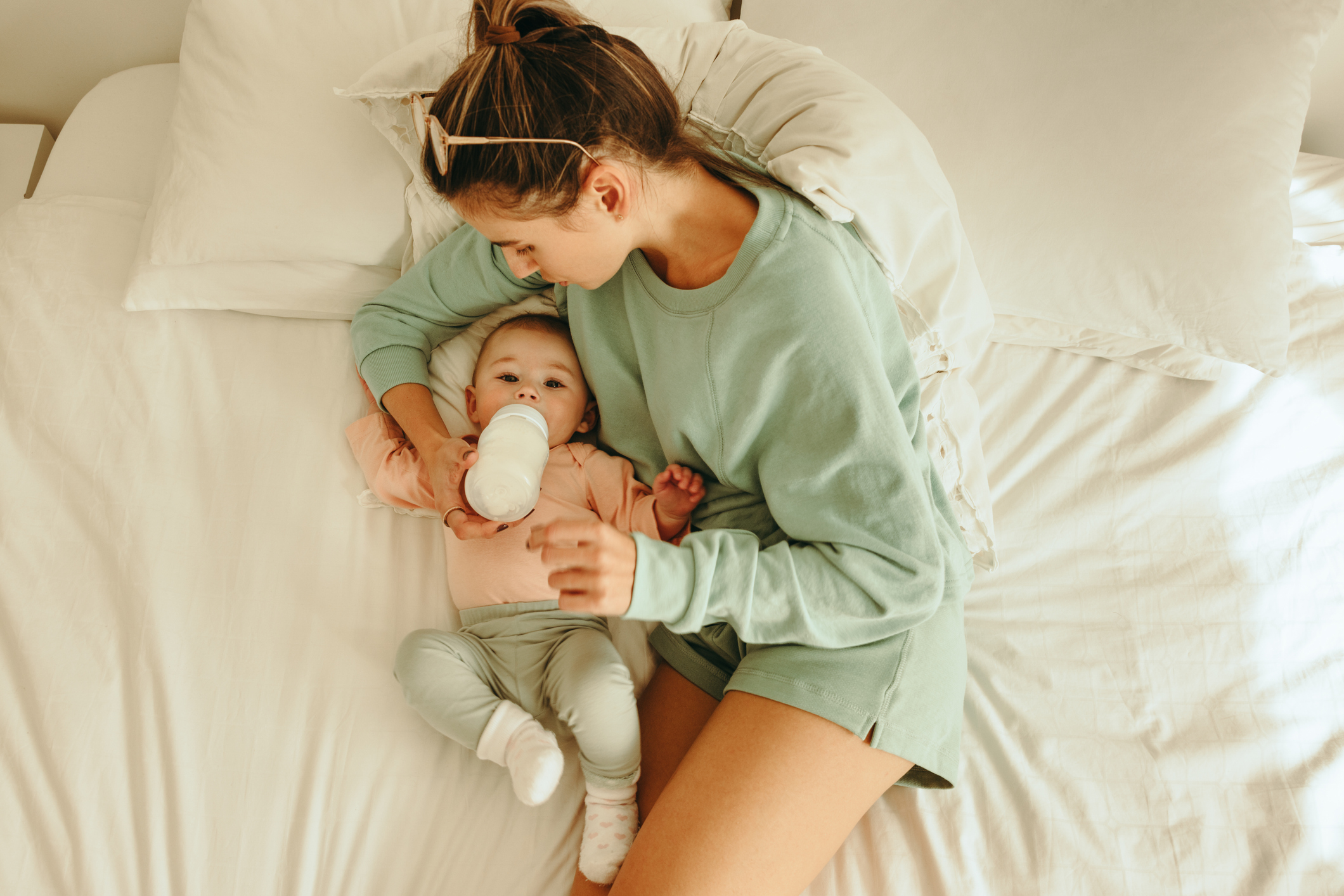Overhead view of a mother feeding her baby Overhead view of a loving mother feeding her newborn baby. High angle view of a new mom giving her baby formula milk while lying on the bed. Single mom caring for her infant child.